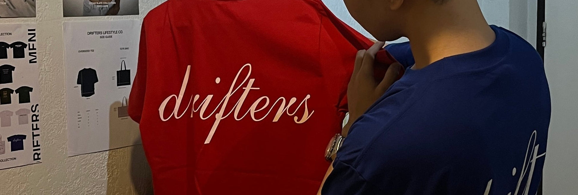 Person wearing a red sweatshirt with 'drifters' branding, standing in a room with a white wall and a window.